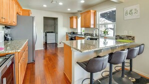 Une cuisine moderne avec des meubles en bois, un plan de travail en granit et un coin bar avec des tabourets.