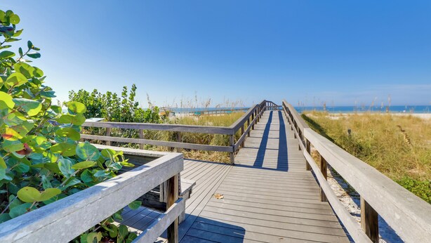 Ein hölzerner Steg führt zu einem Strand, der bewölktem Himmel entgegenblickt.