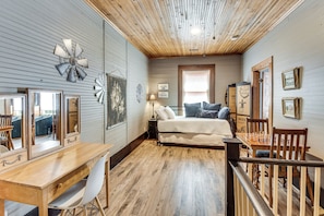 A bedroom with a wooden desk, a bed, a window, and a wooden ceiling.