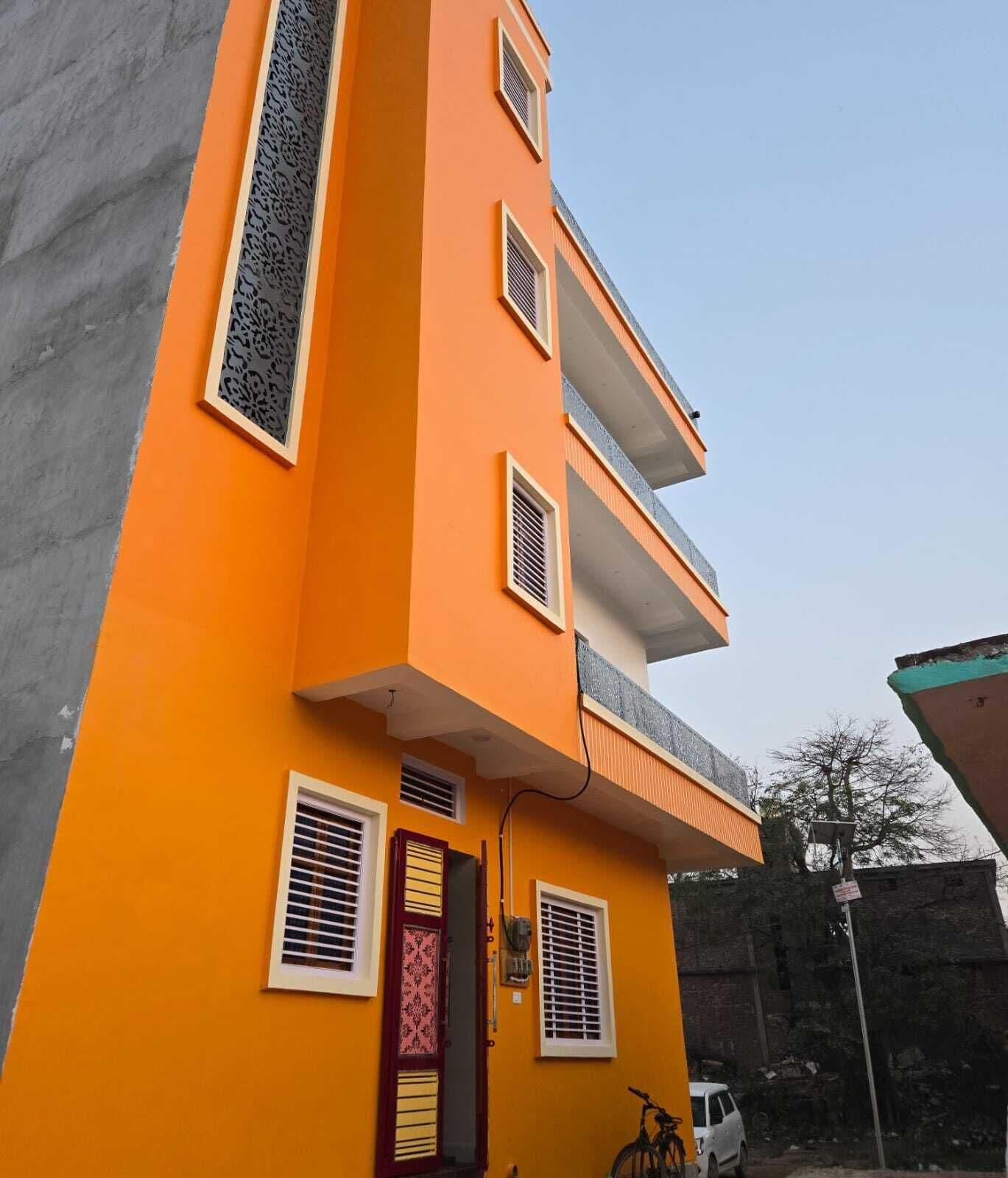 Un edificio a più piani con una facciata giallo-arancio vivace, diverse finestre con persiane e una porta ben visibile con un motivo decorativo.