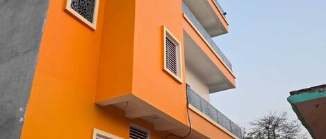 Un edificio a più piani con una facciata giallo-arancio vivace, diverse finestre con persiane e una porta ben visibile con un motivo decorativo.