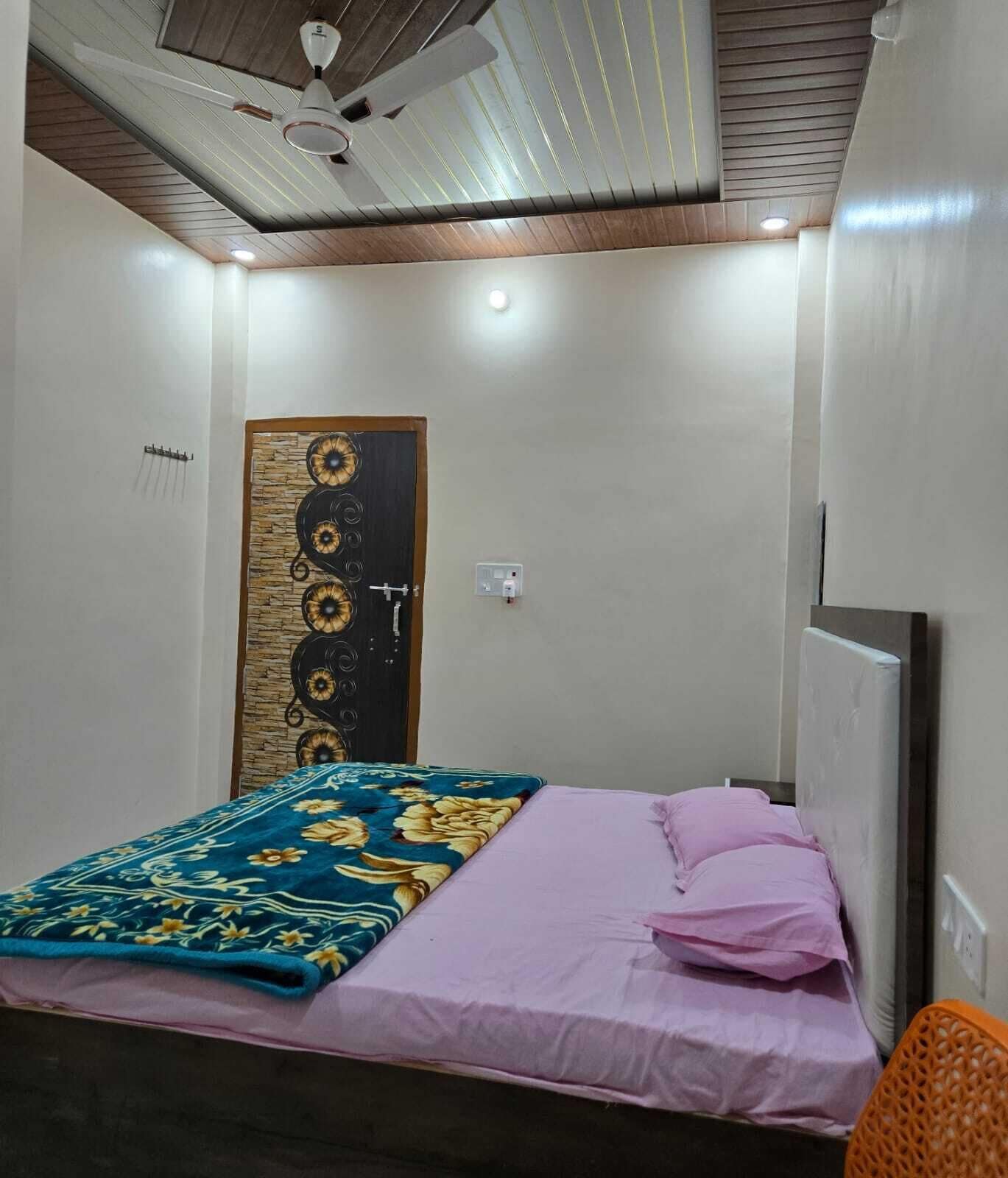 A bedroom with a bed, a ceiling fan, a door with a decorative panel, and a power outlet.