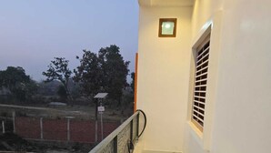 A balcony with a railing, a window with blinds, and a small light fixture. - Hotel Anmol Kothi (Ayodhya)