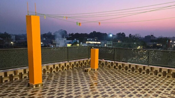 A rooftop terrace with a patterned floor, two orange pillars, and a view of the cityscape at dusk. - Hotel Anmol Kothi (Ayodhya)