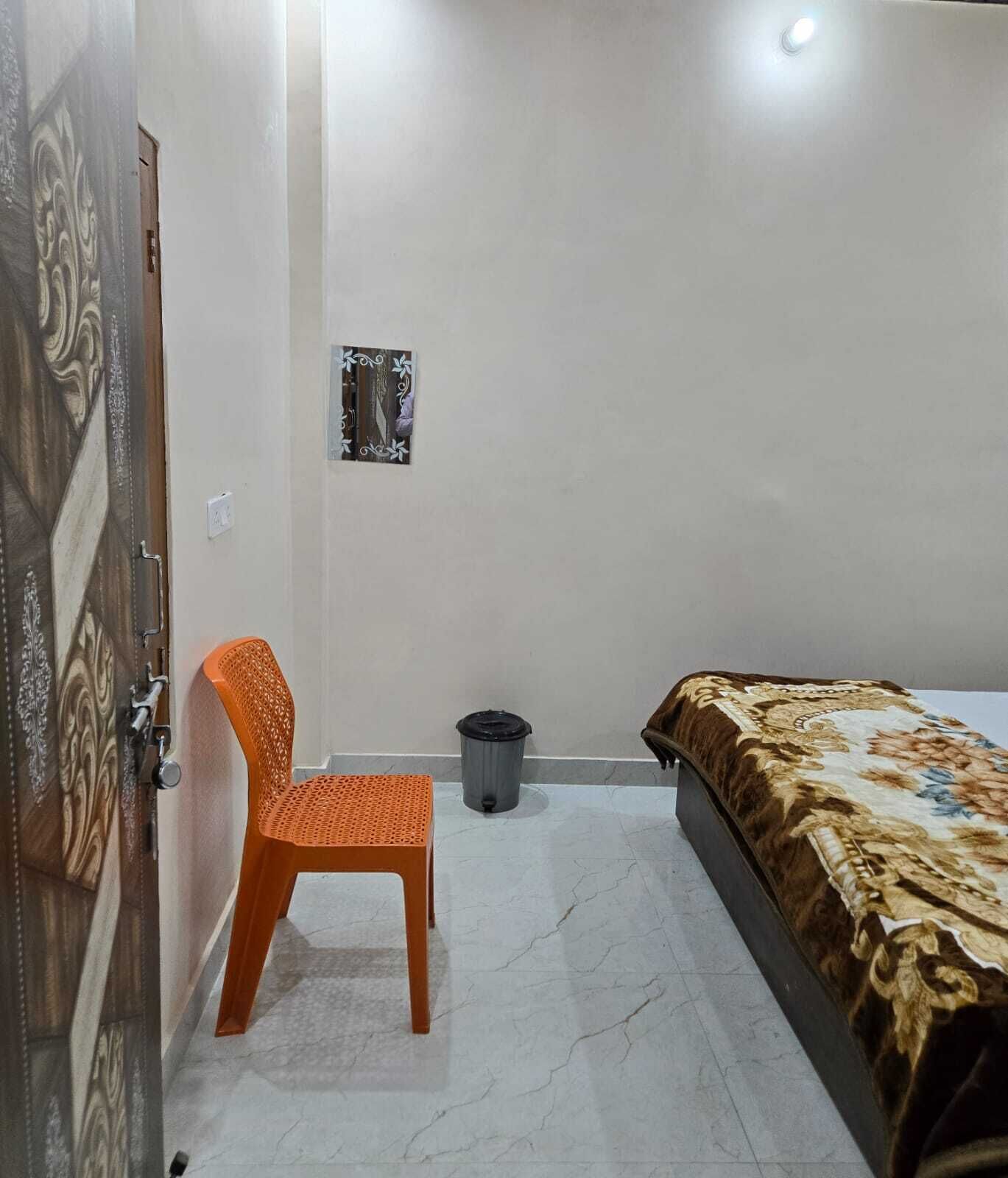 Une chambre à coucher avec un lit, un fauteuil orange, une poubelle et une porte ornée d’un panneau décoratif.