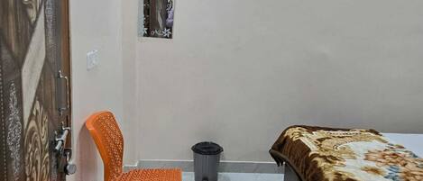 Une chambre à coucher avec un lit, un fauteuil orange, une poubelle et une porte ornée d’un panneau décoratif.