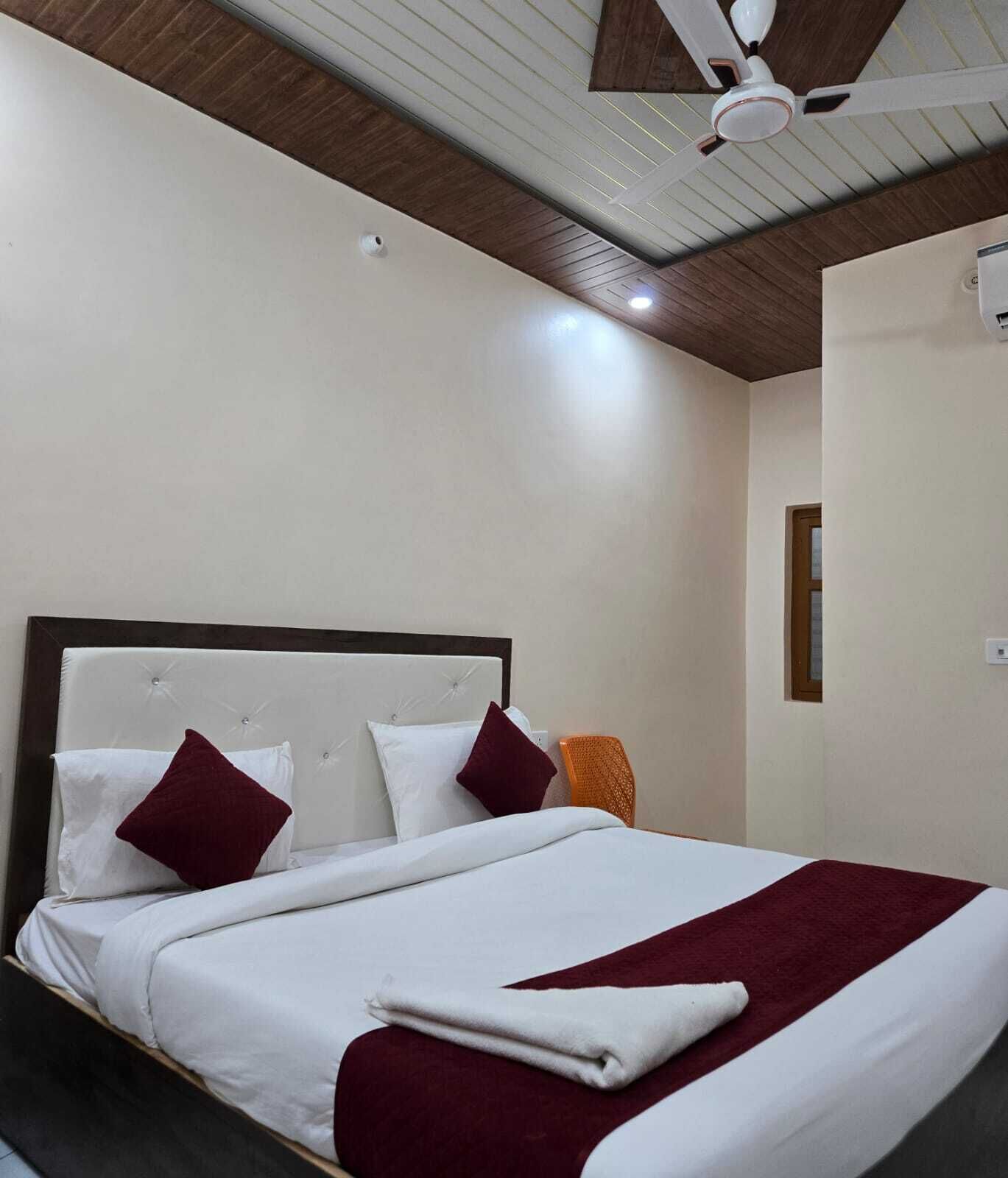 A neatly made bed with white and maroon bedding, a wooden headboard, and a ceiling fan.