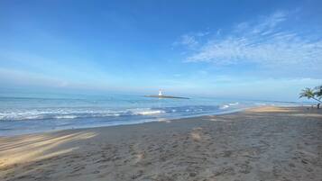 A beach with a lighthouse in the distance, sandy shore, and clear sky.