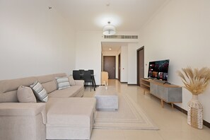 Ein modernes Wohnzimmer mit einer Couch, Hocker, Fernseher und einer dekorativen Vase.