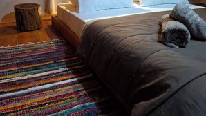 Un dormitorio cálido en el ático, con techo de madera, cama con ropa blanca y una alfombra a rayas colorida.