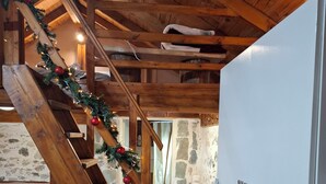 Una escalera de madera adornada con una guirnalda, una cama, una lavadora y un muro de piedra.