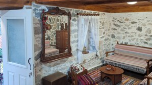 Una habitación rústica con pared de piedra, vigas de madera en el techo, un banco de madera, una pequeña mesa con cerámica y un espejo con marco decorativo.