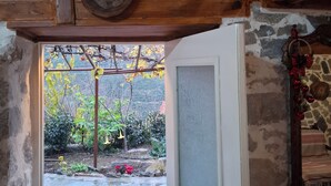 Techo de madera rústica con pared de piedra y puerta que da a un espacio exterior con suelo de piedra y vegetación.