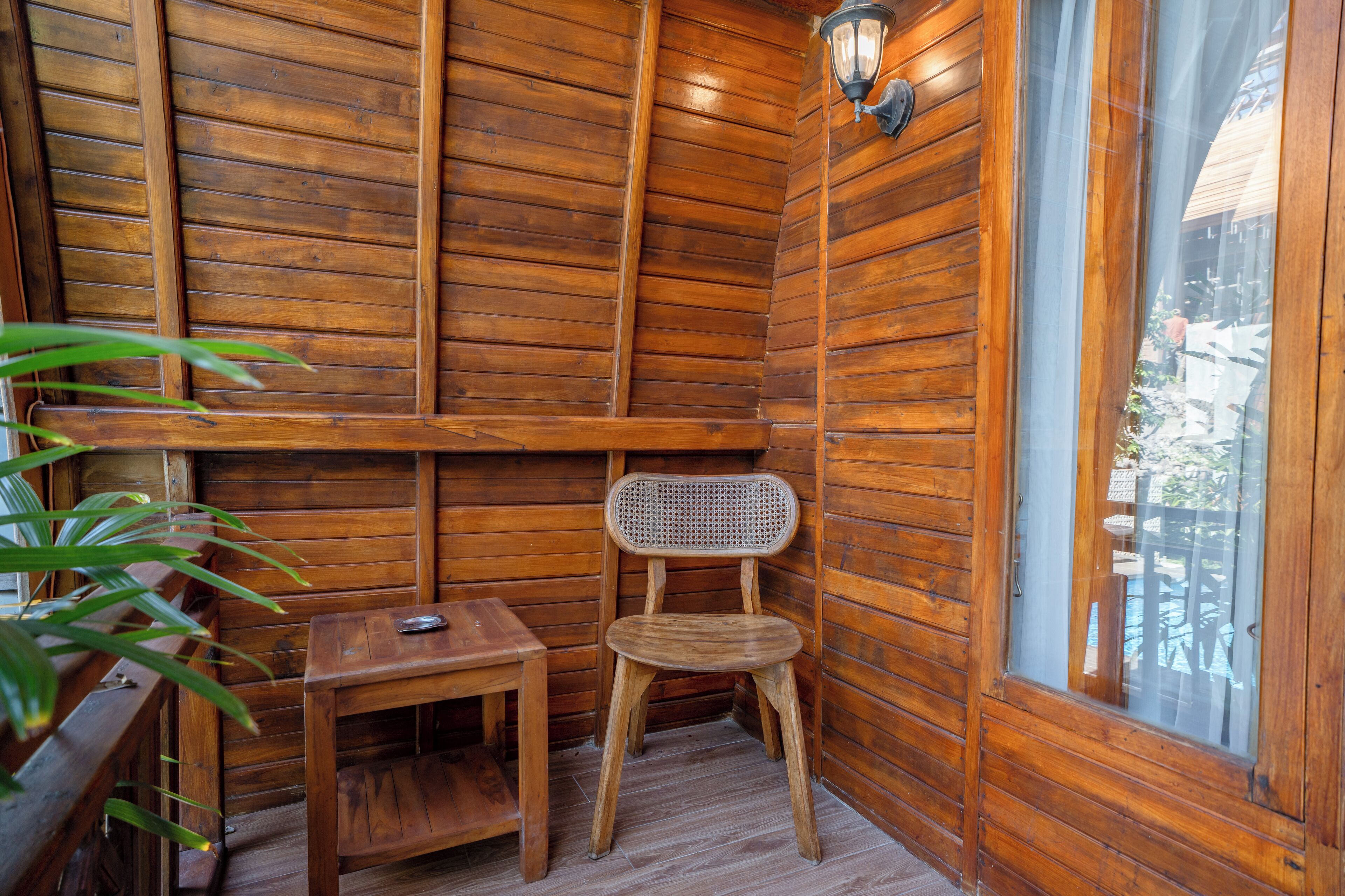 L’intérieur d’un chalet en bois, avec une table en bois, une chaise en osier et une fenêtre donnant sur l’extérieur.