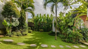 Un jardin luxuriant, avec une grande variété de plantes tropicales, un sentier en pierre et une pelouse bien entretenue.