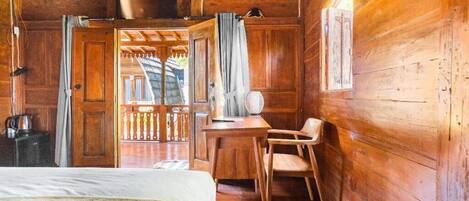 A wooden cabin room with a bed, a desk, a chair, and a window.