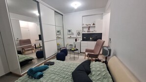 A compact bedroom with a bed, a chair, a small table, a mirror, and a kitchenette. - The studio offers cleanliness, peace and comfort, for a pleasant, relaxing stay! (Pafos)