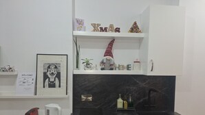 A modern kitchen with a black marble countertop, a built-in stove, and a sink. There are shelves above the stove with decorative items, including a 'XMAS' sign and a small Christmas tree made of bottles. - The studio offers cleanliness, peace and comfort, for a pleasant, relaxing stay! (Pafos)