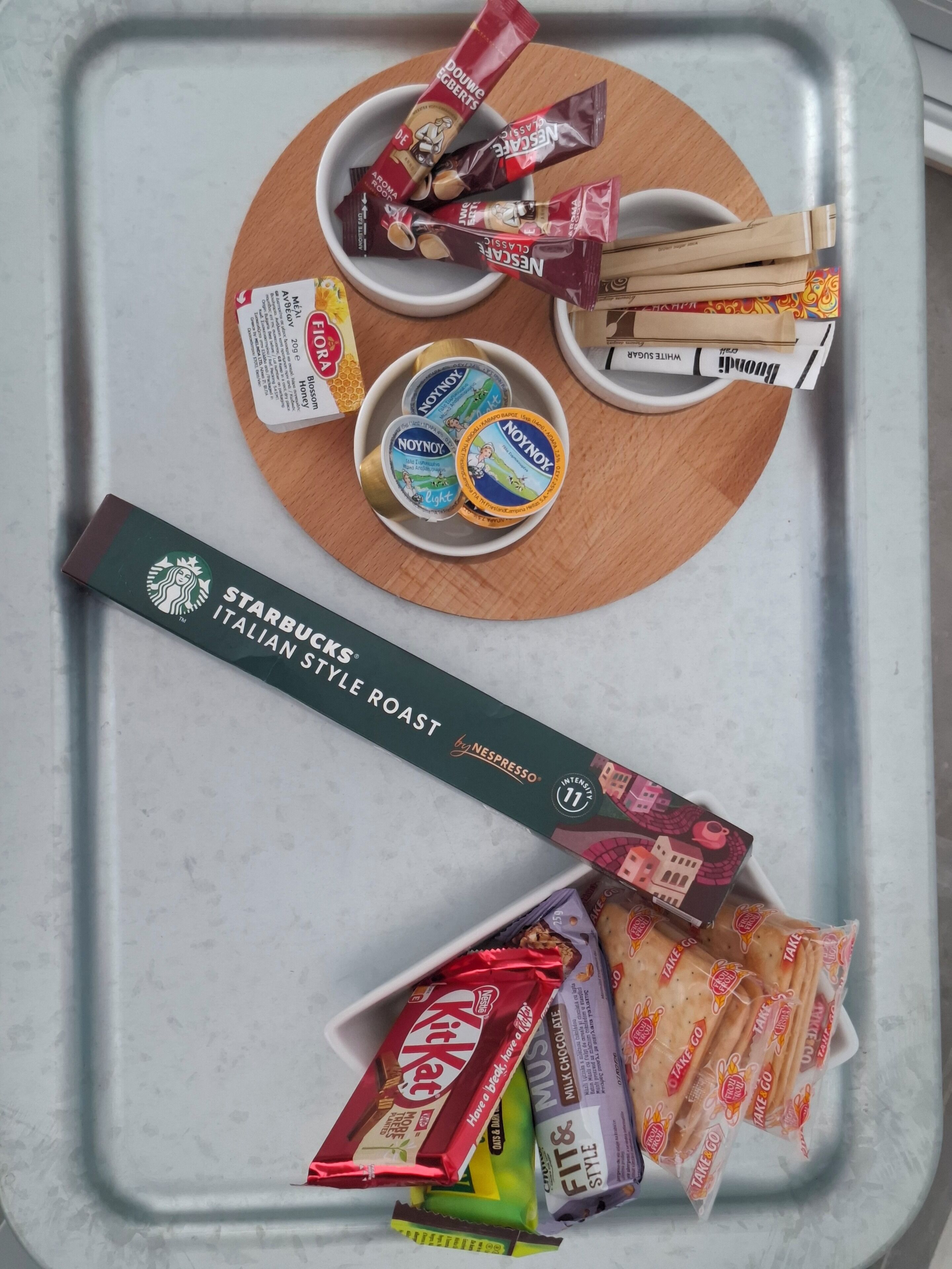 A tray with various food items including Nespresso coffee pods, snacks, and a Starbucks Italian Style Roast coffee box.