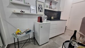A compact kitchen with a refrigerator, a small table with a chair, and a shelf with decorative items. - The studio offers cleanliness, peace and comfort, for a pleasant, relaxing stay! (Pafos)