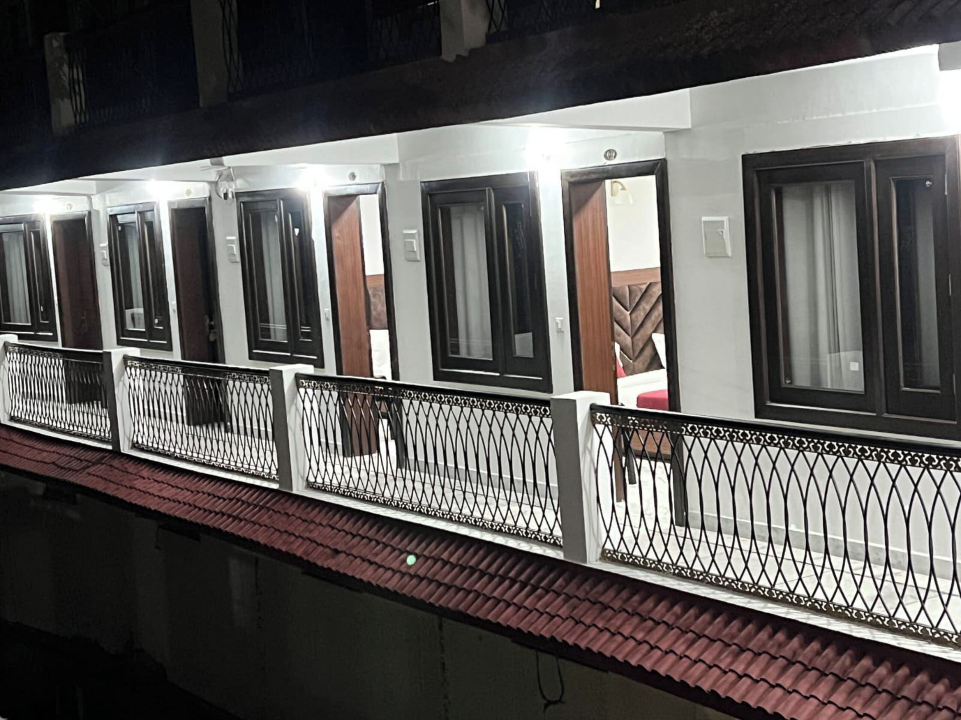 A row of hotel rooms with individual doors, a balcony with a metal railing, and a tiled roof.