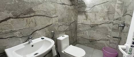 A bathroom with a sink, toilet, shower, and a small window.
