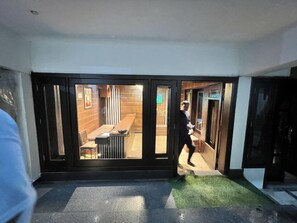 L’entrée d’un hôtel, avec un comptoir d’accueil, un espace d’attente doté d’un banc, et une personne qui traverse les portes.