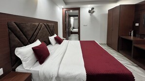 Ein Hotelzimmer mit einem großen Bett, einem Holzkopfteil und einem roten Zierkissen. Es gibt einen Kleiderschrank und einen Schreibtisch mit einer Lampe.
