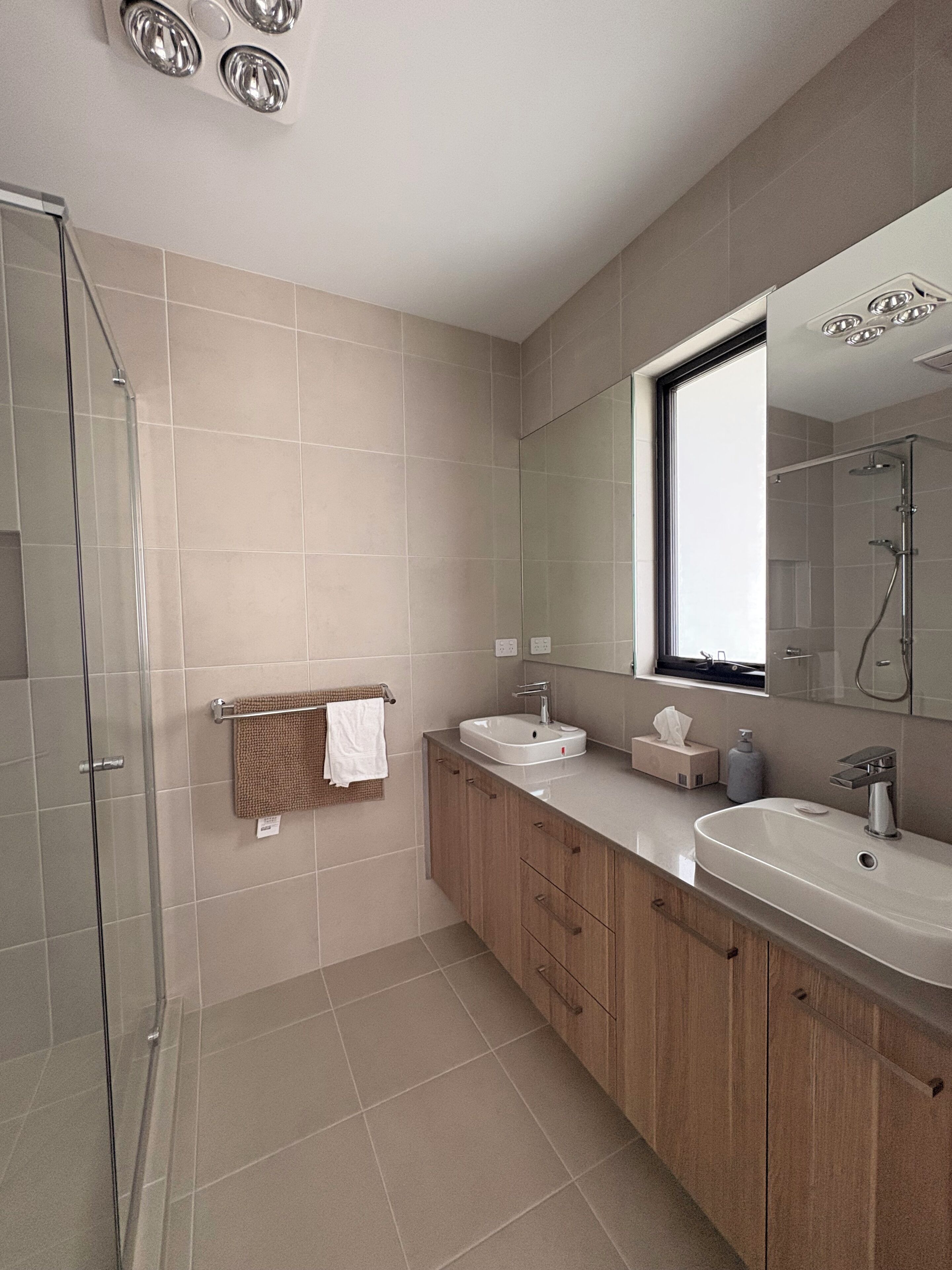 Ein modernes Badezimmer mit einer Duschkabine aus Glas, zwei Waschbecken, einem großen Spiegel und Holzschränken.