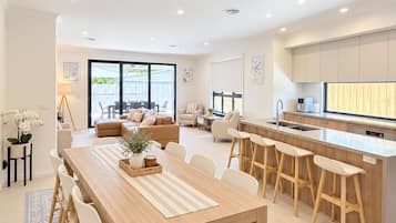 A modern kitchen with a central island, a dining area with a wooden table and chairs, and a living area with a sofa and chairs.