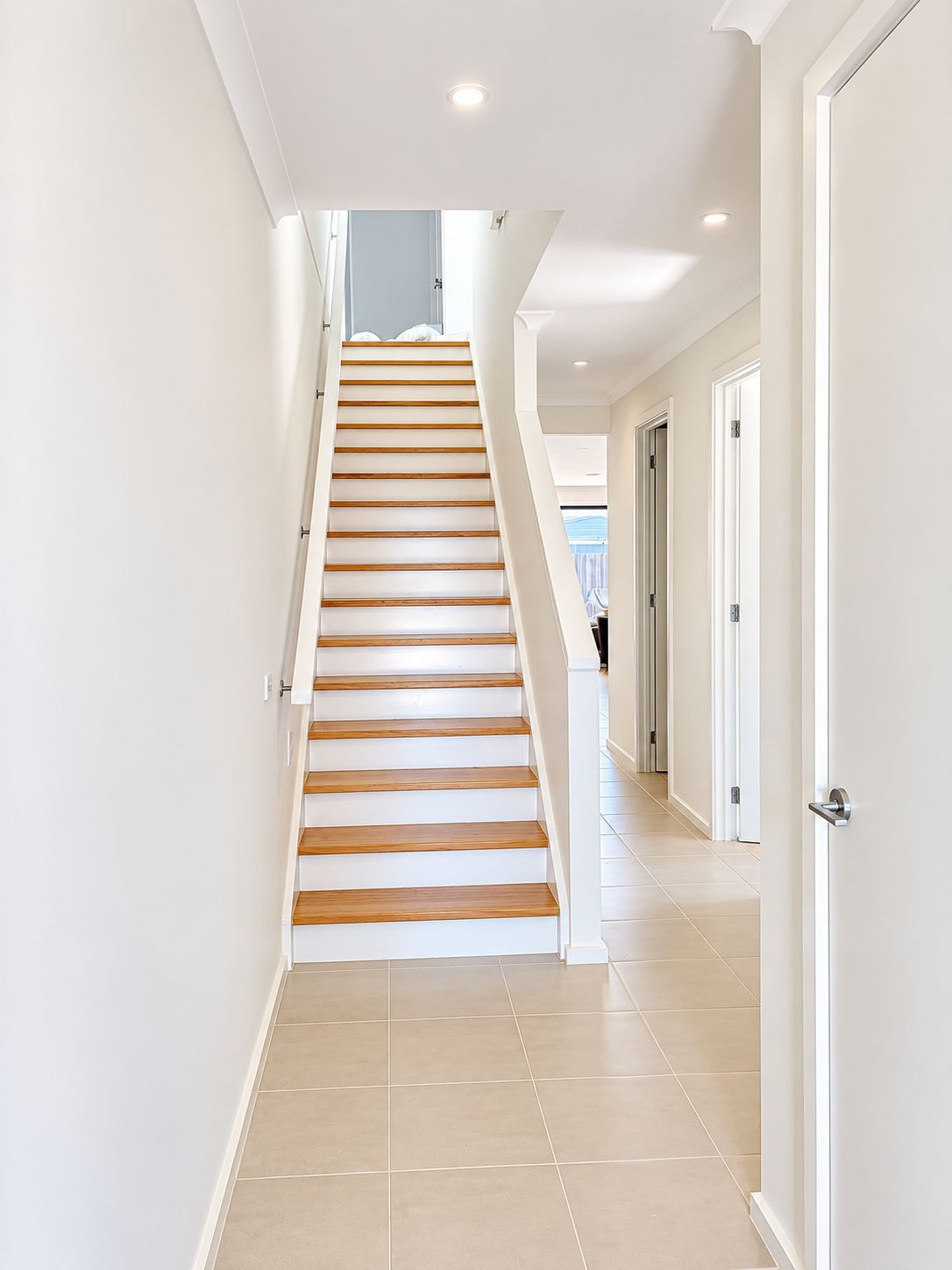 A staircase with wooden steps leading to a landing, surrounded by white walls and doors.