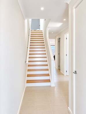 A staircase with wooden steps leading to a landing, surrounded by white walls and doors. - Cowes Family Retreat | Walk to beach, shops & cafes - Sleeps up to 14 (Cowes)