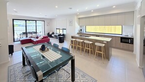 Eine moderne Küche mit einer zentralen Kochinsel, Barhocker und einem Essbereich mit Glastisch und Stühlen.