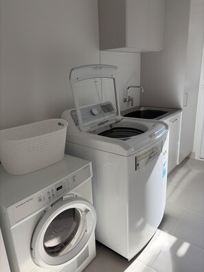Ein Waschraum mit einer Frontlader-Waschmaschine und einem Trockner, einem Wäschekorb und einem Waschbecken.