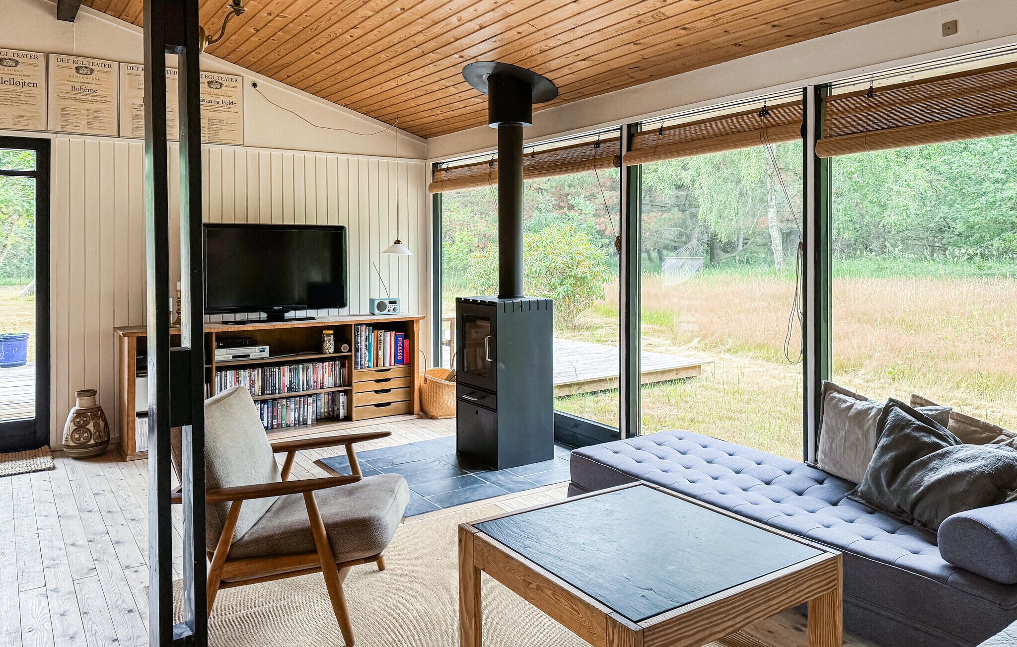 Uma sala de estar moderna com televisão, estantes, um sofá e uma grande janela com vista para uma paisagem natural.