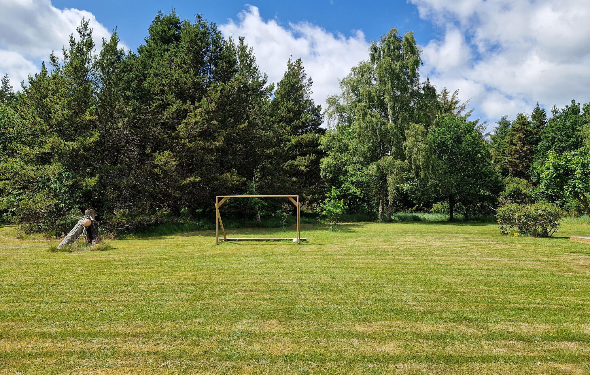 A grassy field with a wooden swing set and a tree in the background.