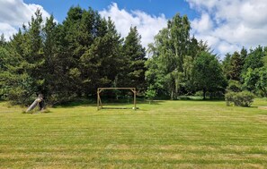 Um campo gramado com um balanço de madeira e uma árvore ao fundo.