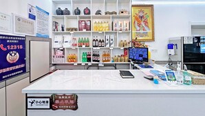 Een receptiebalie met een computerscherm, een telefoon en diverse voorwerpen op de toonbank. Achtergrond toont planken met flessen en decoratieve objecten.