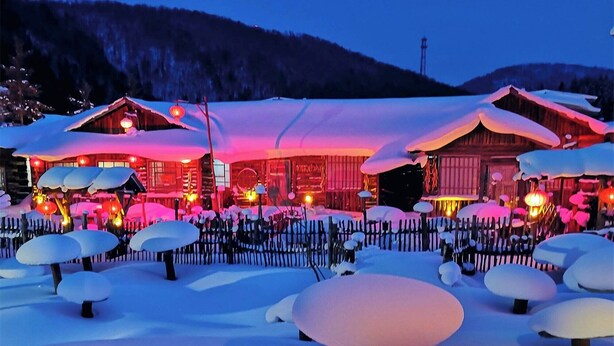 Een besneeerd landschap met een houten gebouw, grote ramen en een sneeuwbedekte kap.