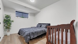 A bedroom with a bed, a crib, a potted plant, and a window with blinds. - 2 bedroom suite with 3 beds, close to Amenities and Airport (Leduc)