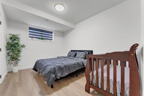 A bedroom with a bed, a crib, a potted plant, and a window with blinds. - 2 bedroom suite with 3 beds, close to Amenities and Airport (Leduc)