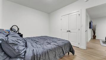A bedroom with a bed, a nightstand, a TV, and a door leading to another room.