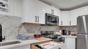 A modern kitchen with white cabinets, a stainless steel refrigerator, a microwave, and a stove. - 2 bedroom suite with 3 beds, close to Amenities and Airport (Leduc)
