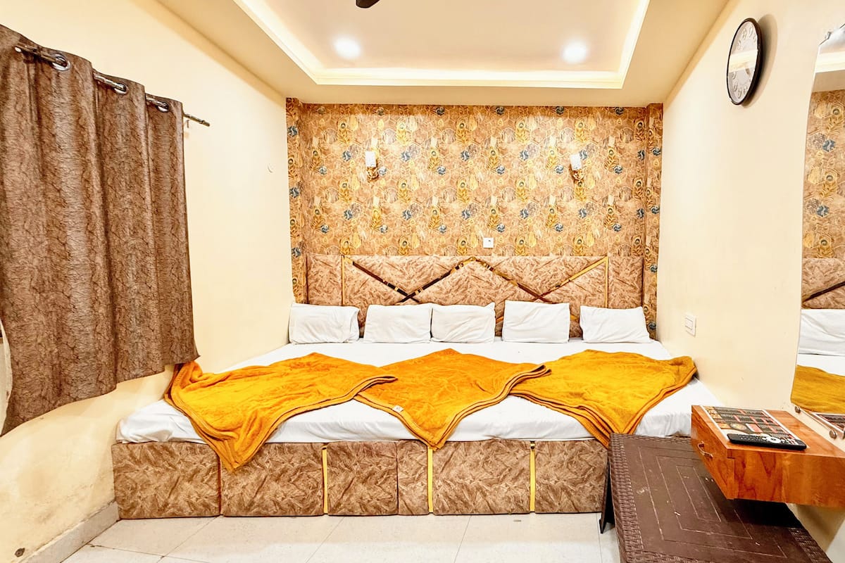 A bedroom with a patterned headboard, a bed with white linens and a yellow throw, a wooden nightstand, and a mirror on the wall.
