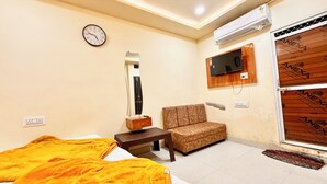 A room with a bed, a chair, a TV mounted on the wall, an air conditioning unit, and a wooden door. - Premium Hotel Sipra near Mahakal Temple  (Ujjain)