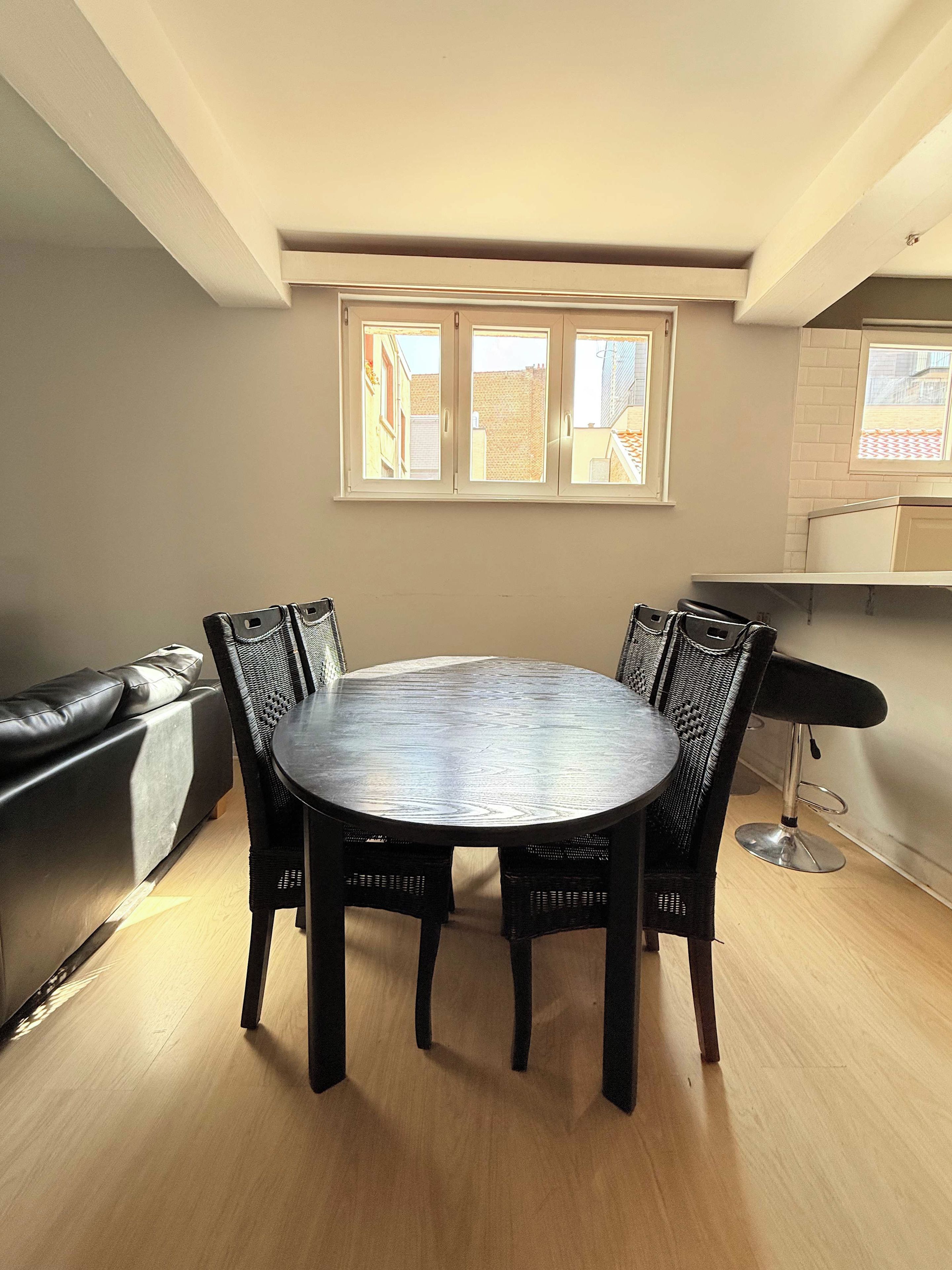 A dining area with a round table and chairs, a sofa, and a window with a view of buildings.