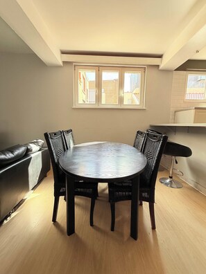 Un coin repas avec une table ronde et des chaises, un canapé et une fenêtre donnant sur des immeubles.