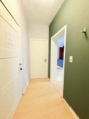 A hallway with a white door, a green wall, and a wooden floor. - Stay in the Heart of Brussels – Steps from Grand Place & Manneken Pis (Brussels)