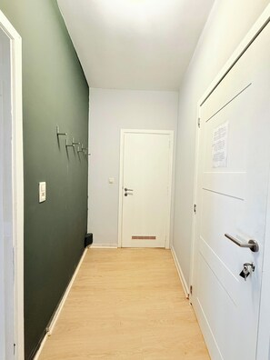 Un couloir avec un mur vert, une porte blanche et un plancher en bois.