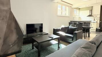 A modern living room with a sofa, a coffee table, and a TV. There is a dining area with a table and chairs.